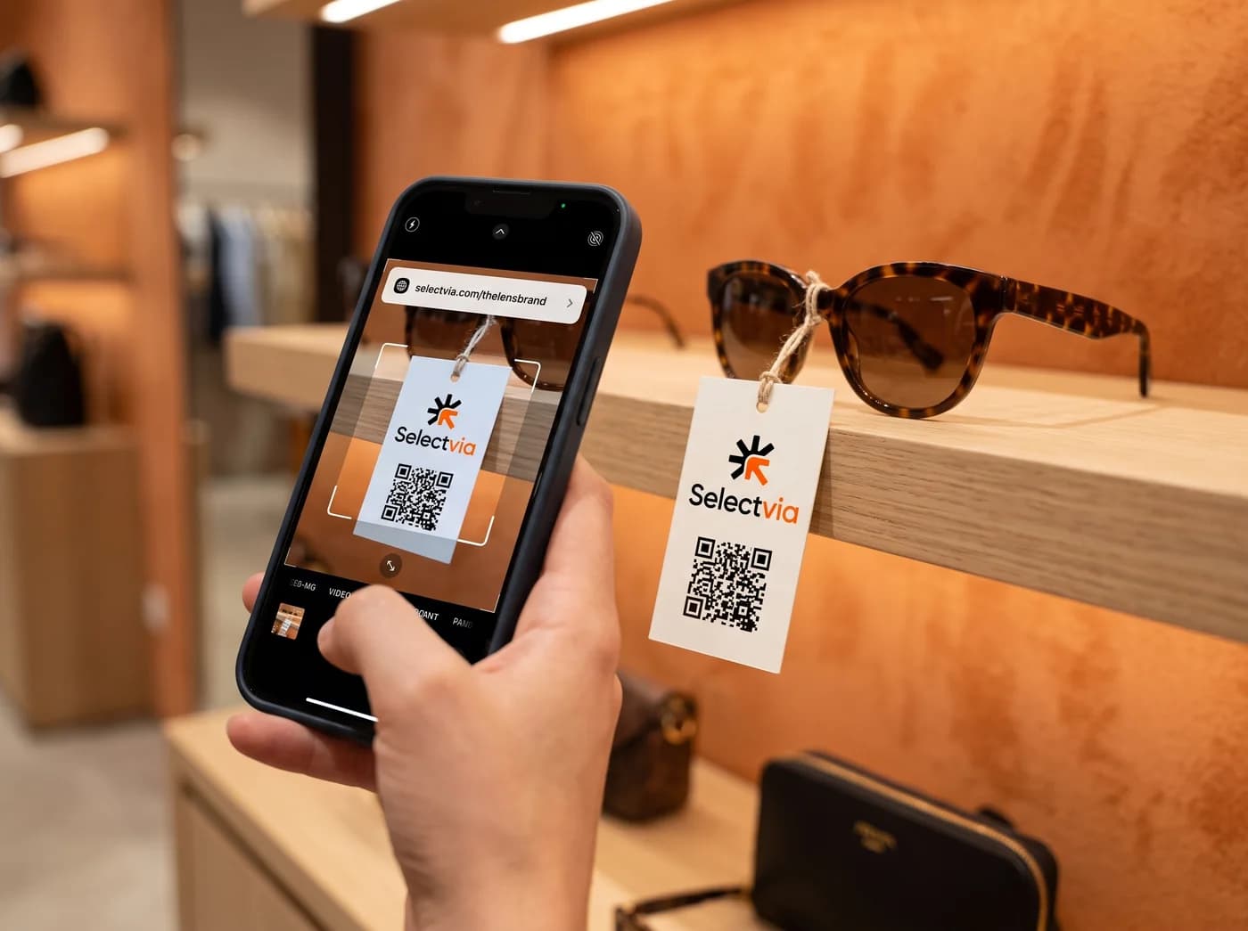 A shopper scanning a Selectvia QR hang tag on sunglasses in a boutique